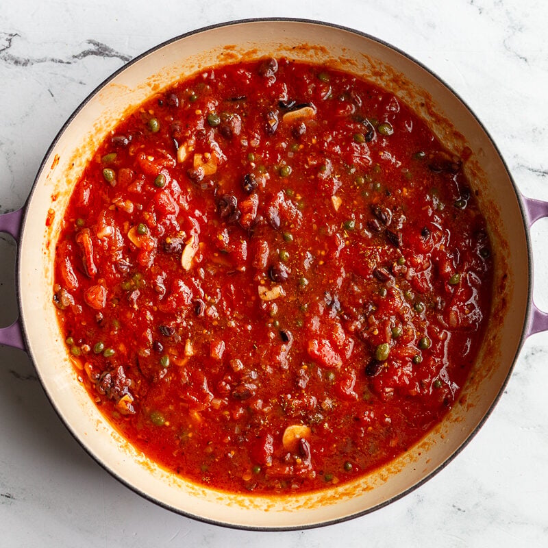 Puttanesca tomato sauce simmering in a skillet with olives and capers.