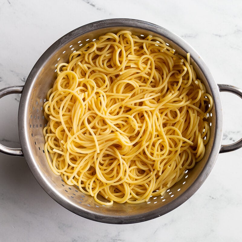 Cooked spaghetti draining in a colander.
