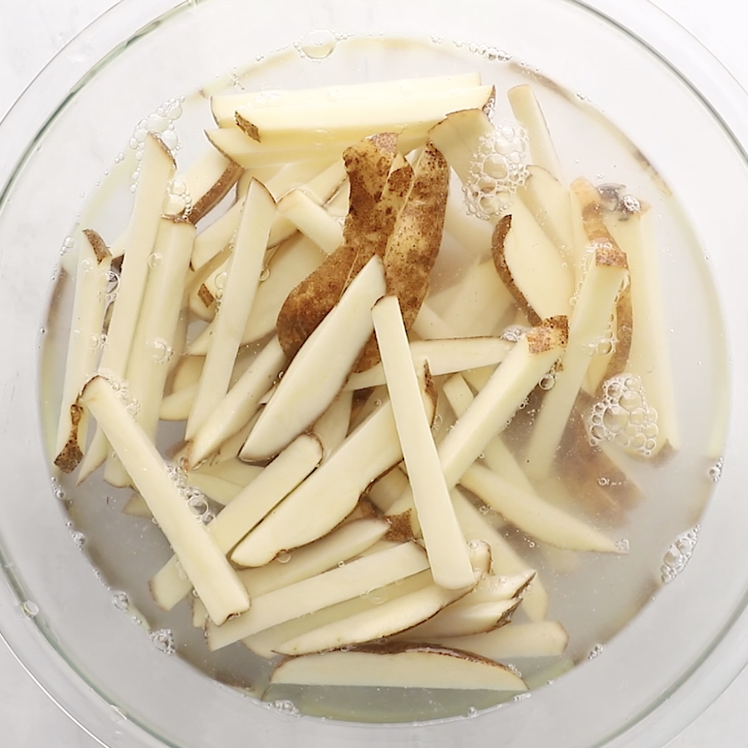cut potatoes in the shape of fries in a bowl of water