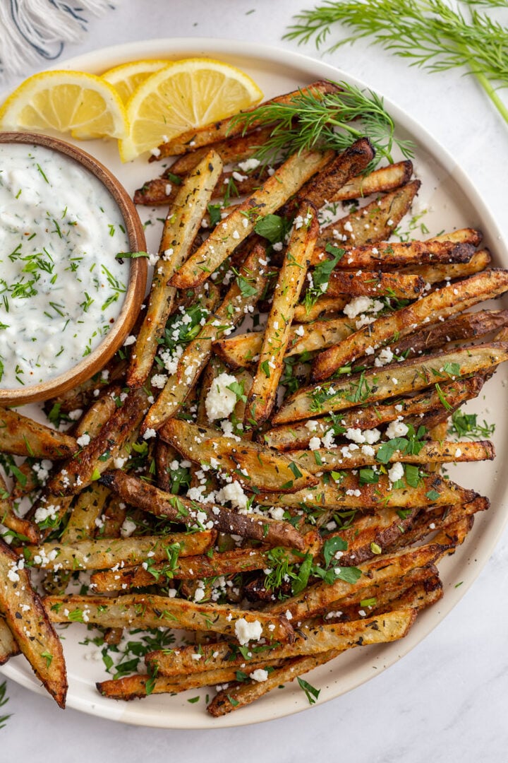 Greek fries on a large plate served with a bowl of dipping sauce