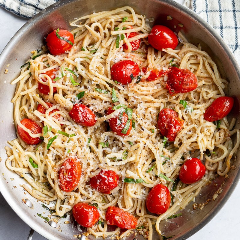 Pasta noodles and cherry tomatoes cooked in a large skillet.