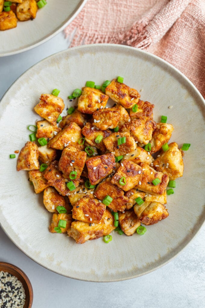 crispy pan fried tofu chunks on a plate with green onion