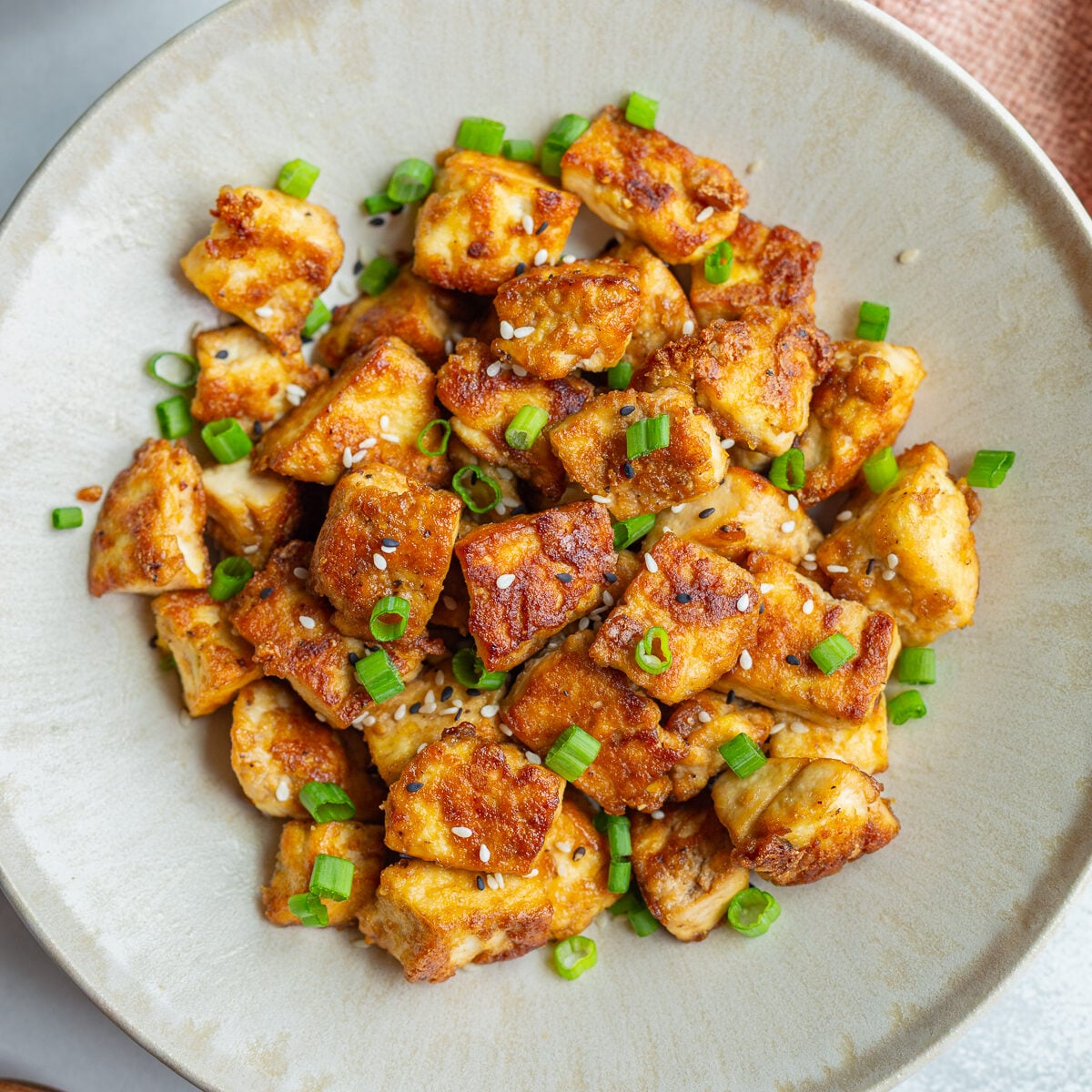 crispy pan fried tofu chunks on a plate with green onion