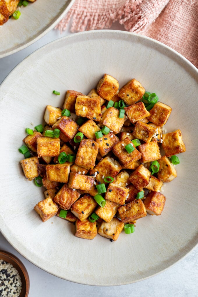 crispy pan fried tofu cubes on a plate with green onion