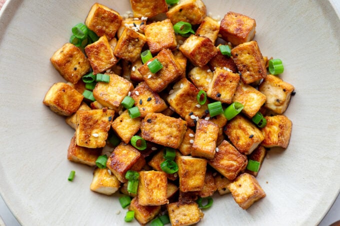crispy pan fried tofu cubes on a plate with green onion