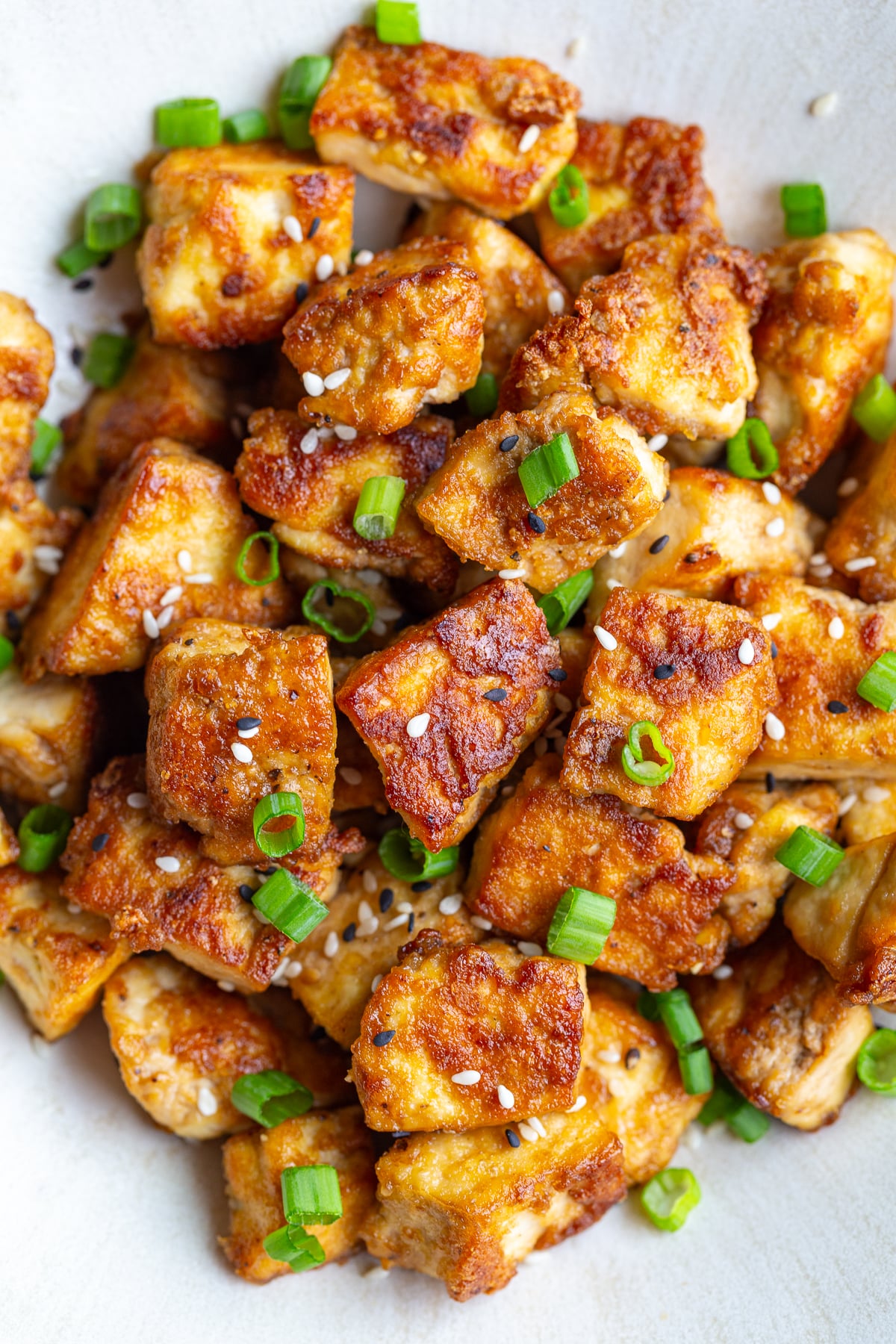 up close shot of crispy pan fried tofu chunks on a plate with green onion