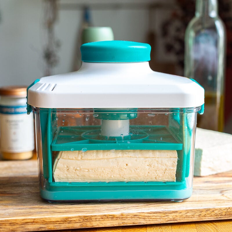 tofu in a tofu press with olive oil and soy sauce in the background