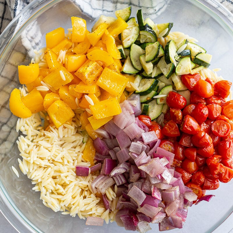Tossing orzo pasta with roasted veggies in a large bowl.