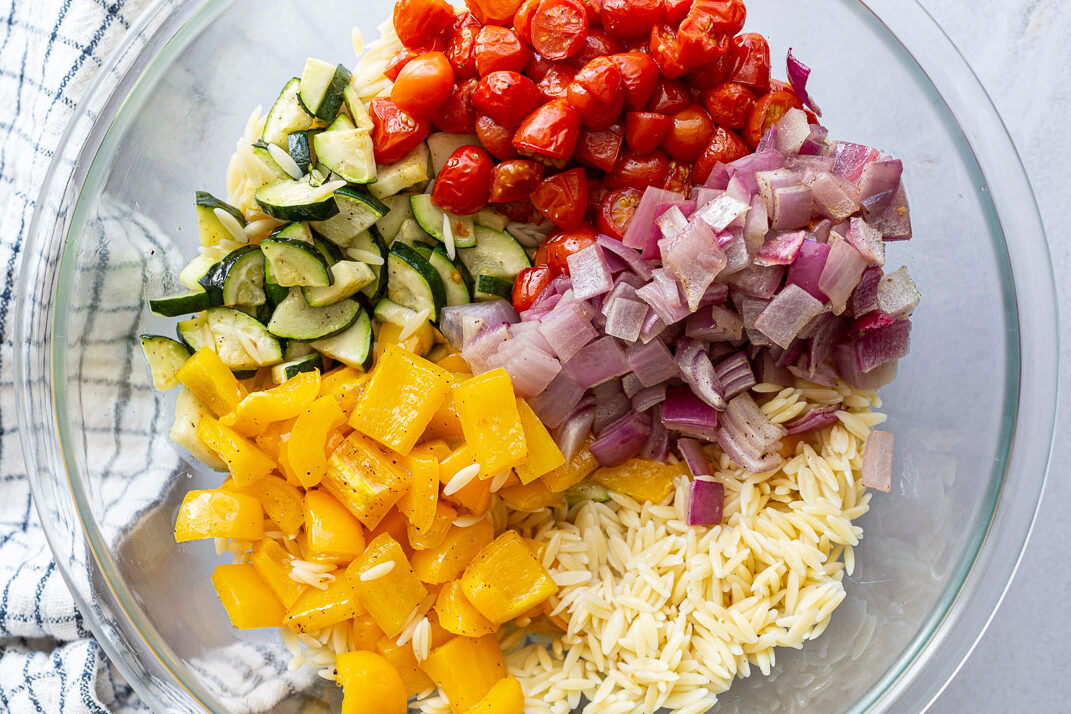 Tossing orzo pasta with roasted veggies in a large bowl.