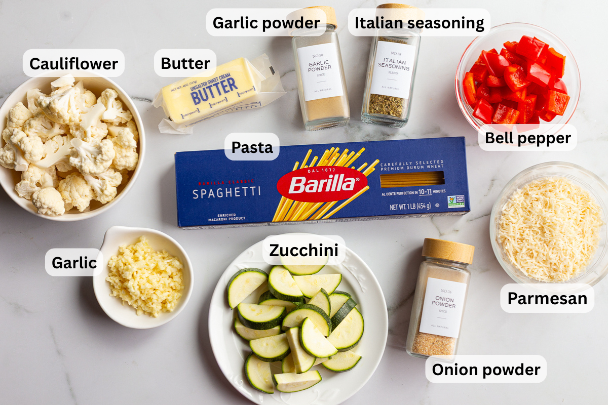 Overhead shot of garlic butter noodles ingredients labeled individually, including cauliflower, butter, garlic powder, Italian seasoning, bell pepper, spaghetti, minced garlic, zucchini, onion powder, and shredded parmesan.