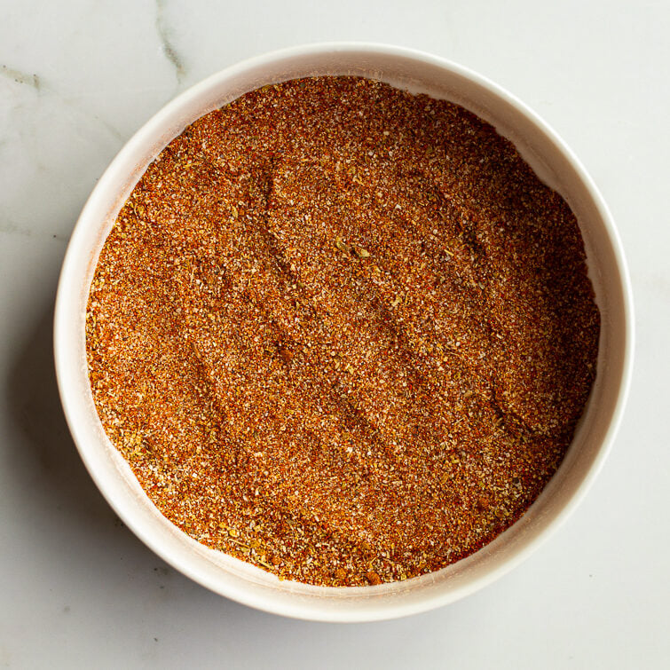 Homemade fajita seasoning fully blended together in a white bowl on a white marble surface, showing a rich red-brown spice mixture ready to use or store.
