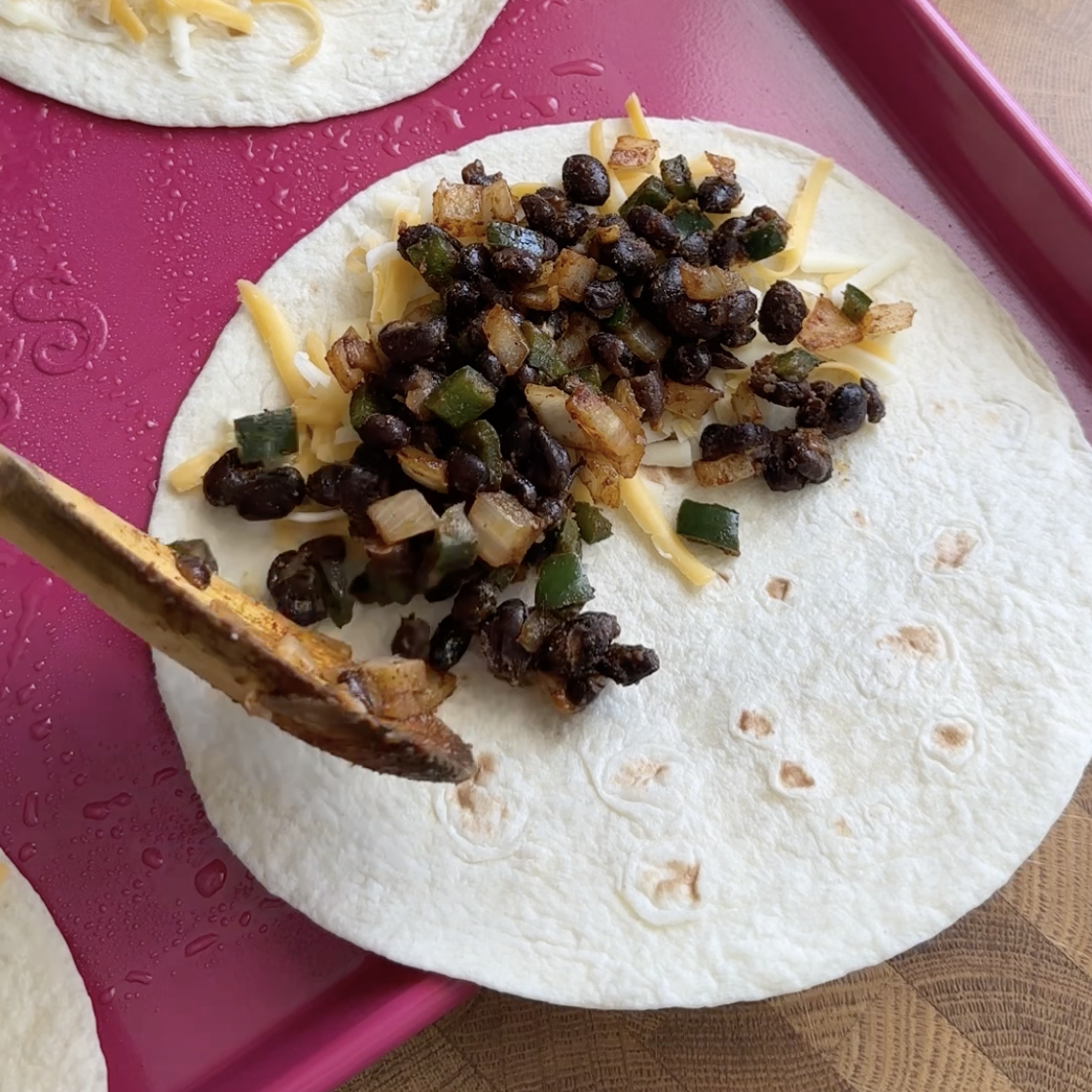 cheeses and black beans being poured onto a flour tortilla