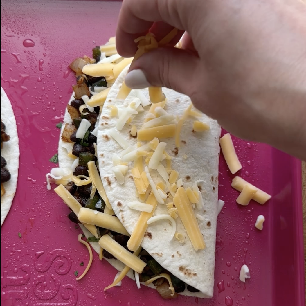 cheese being placed on top of a black bean burrito before its baked