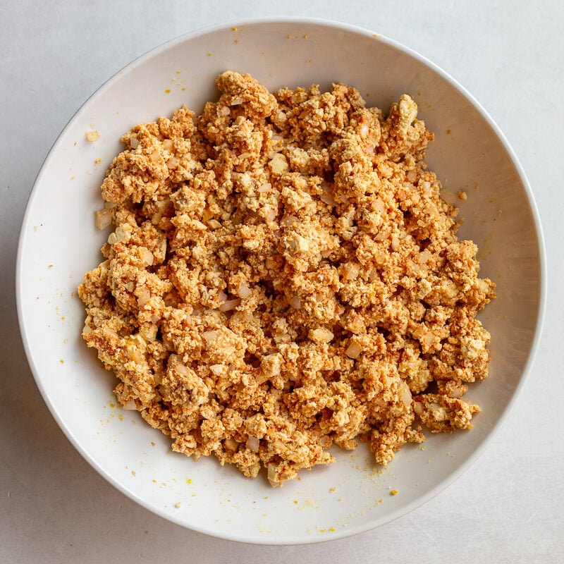 Tofu meatball mixture combined with onion, tomato paste, and seasonings in a bowl.