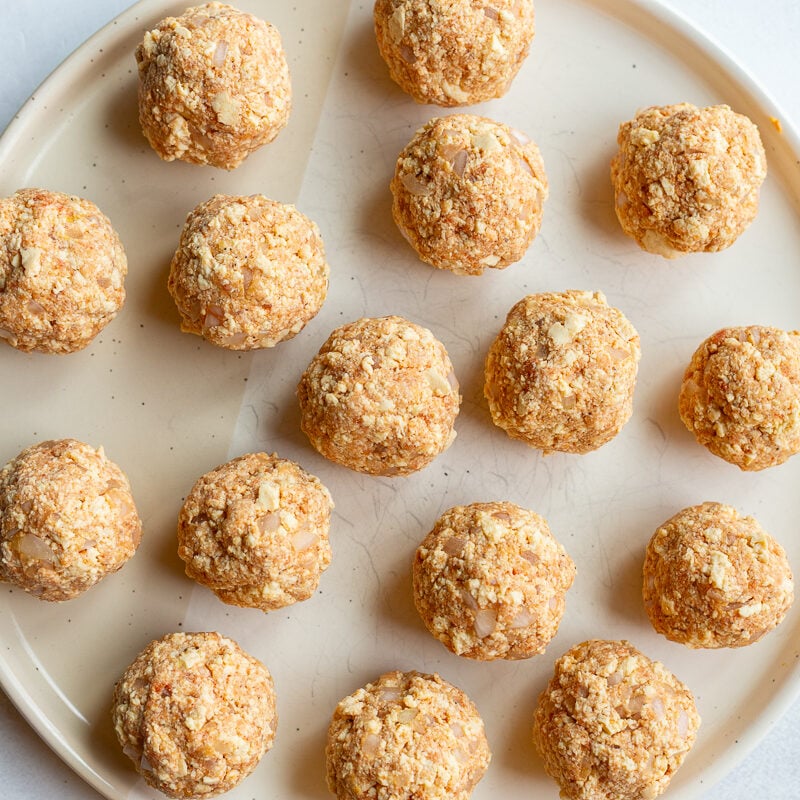 Rolled tofu meatballs arranged on a plate before cooking.