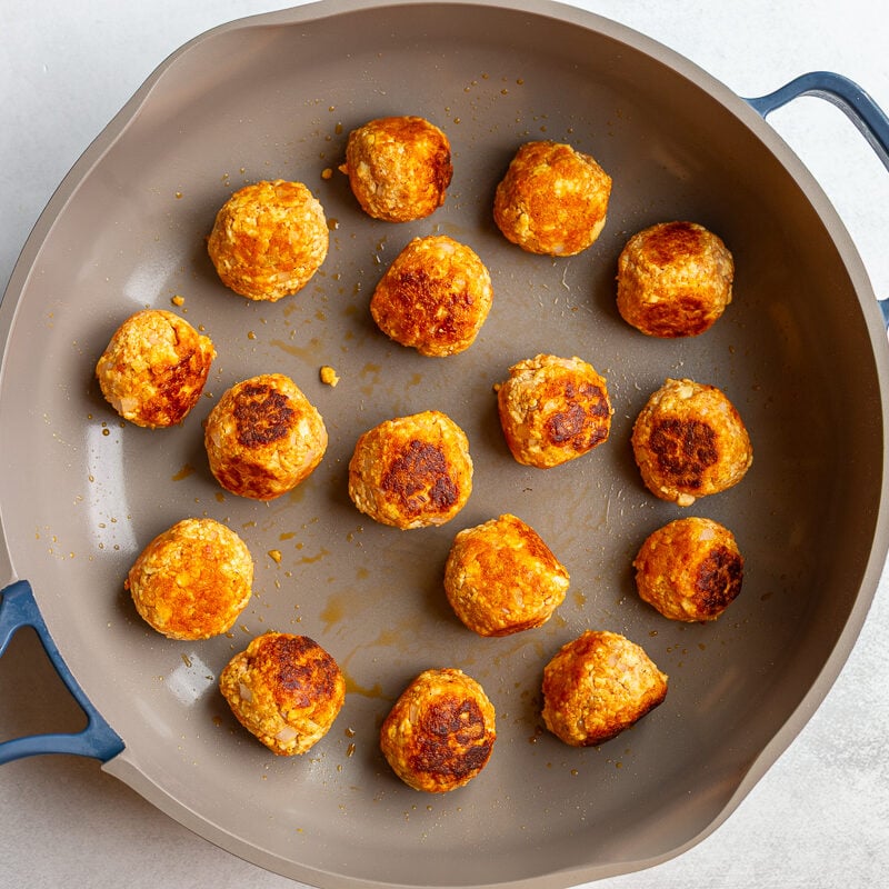 Tofu meatballs searing in a skillet until golden brown on several sides.