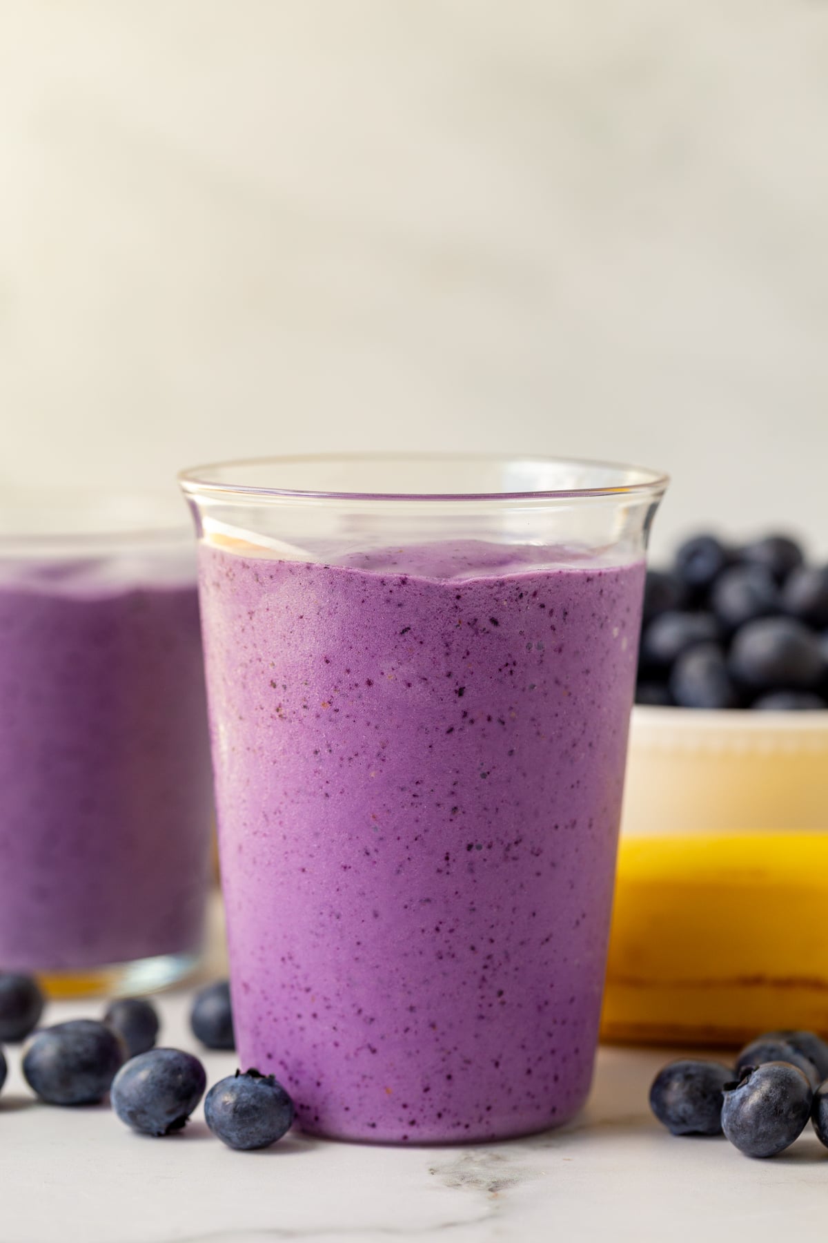 blueberry smoothie in a medium clear glass with blueberries and bananas in the background