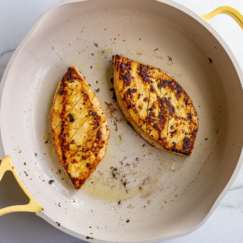 Two triangular slices of tofu seared golden brown with charred edges in a cream-colored skillet.