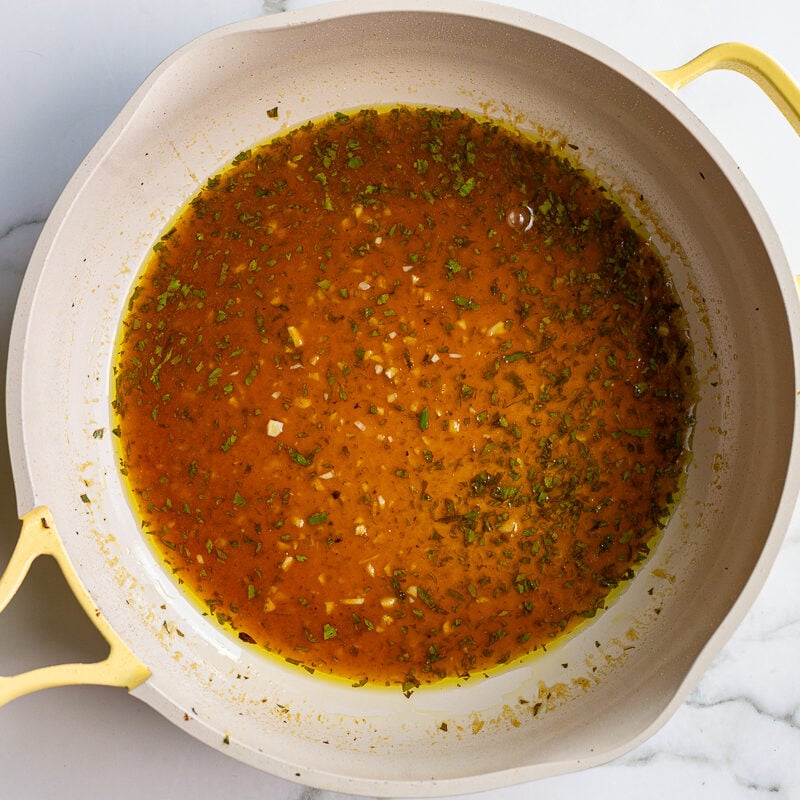 Cilantro lime pan sauce simmering and reducing in a skillet, with flecks of garlic and herbs visible.