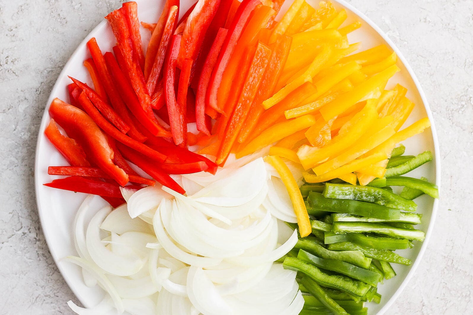 Colorful sliced bell peppers and onion on a white plate.
