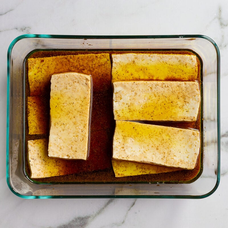 slabs of tofu marinating in a glass dish