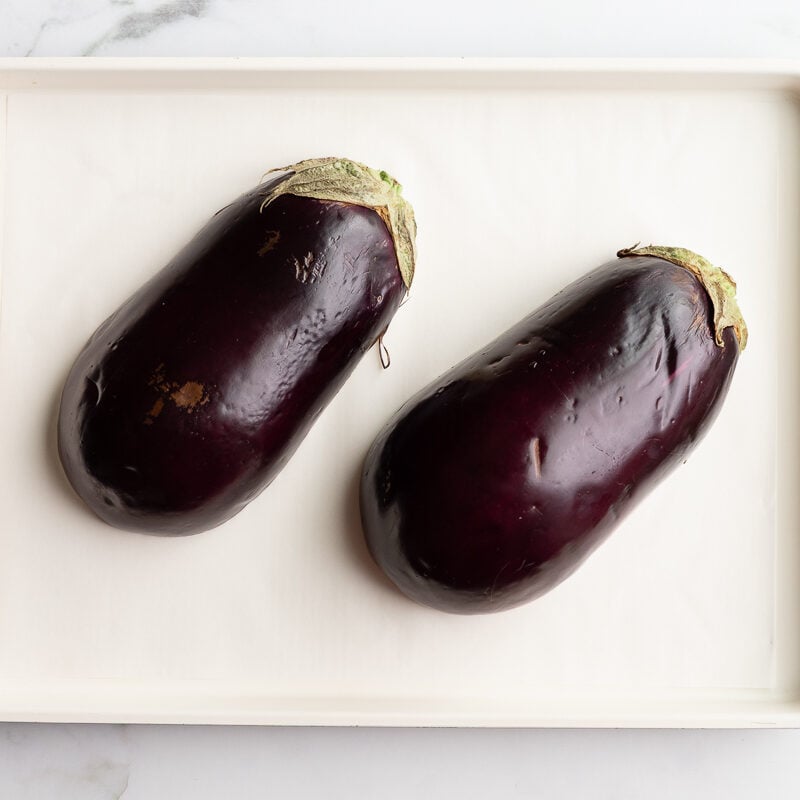 one eggplant halved lengthwise on a parchment-lined baking sheet before roasting
