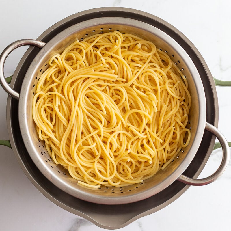 Cooked spaghetti noodles draining in a colander after boiling.