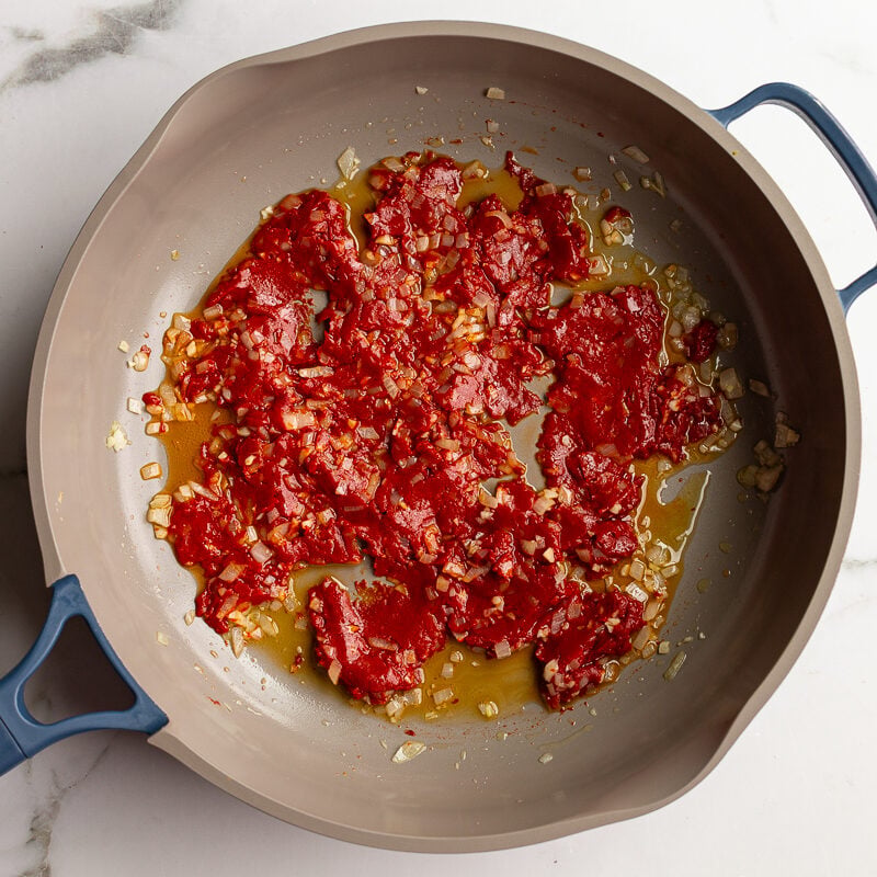 Tomato paste, garlic, and shallot cooking together in a skillet.