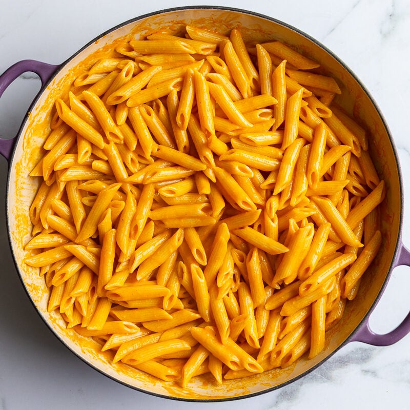 Penne pasta fully coated in creamy roasted red pepper sauce in a skillet