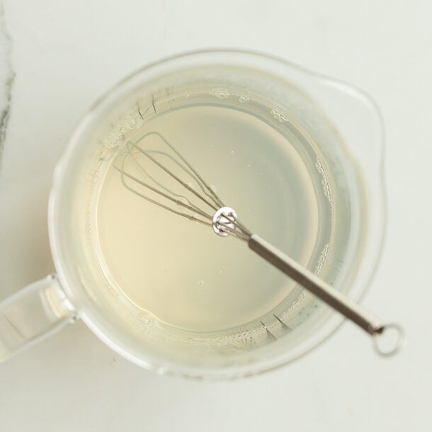 Whisked pectin and water mixture in a glass measuring cup on a marble counter