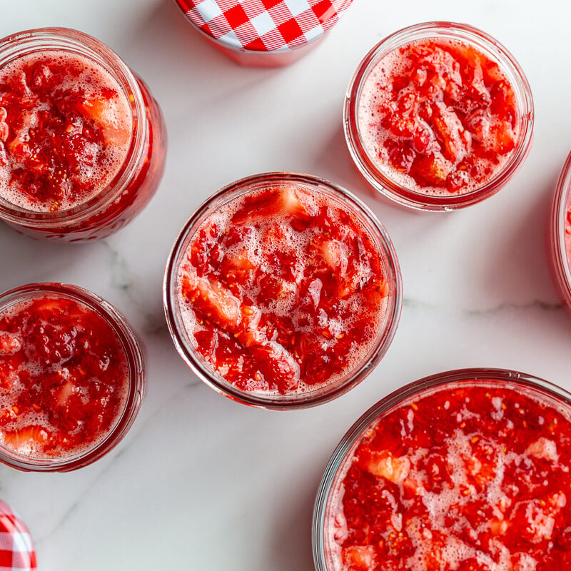 Strawberry freezer jam poured into small glass jars with red gingham lids