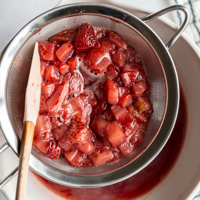 straining cooked strawberries through a fine mesh sieve