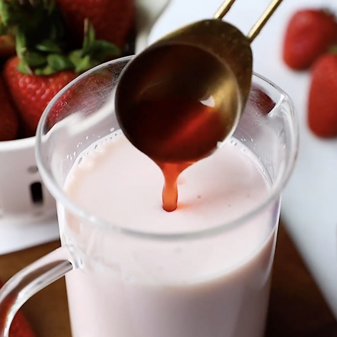 pouring strawberry syrup into a glass of milk to make strawberry milk