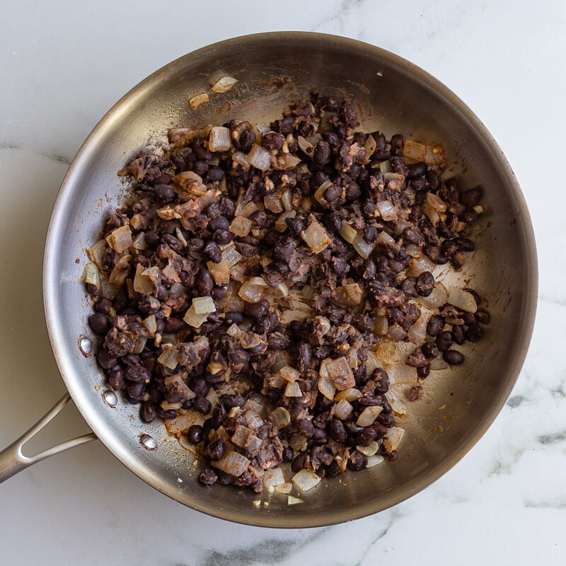 sauteed black beans and onion in a stainless steel skillet
