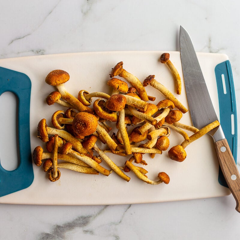 Raw chestnut mushrooms on a cutting board next to a knife, ready to be sliced