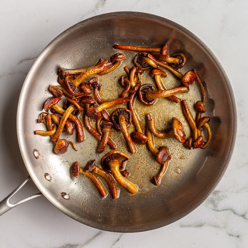 Chestnut mushrooms sautéing in a stainless steel skillet, browning around the edges