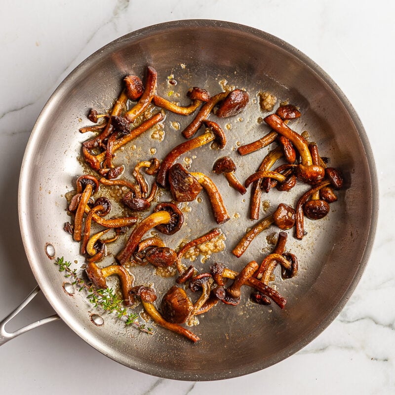 Caramelized chestnut mushrooms in a skillet with fresh thyme sprigs added