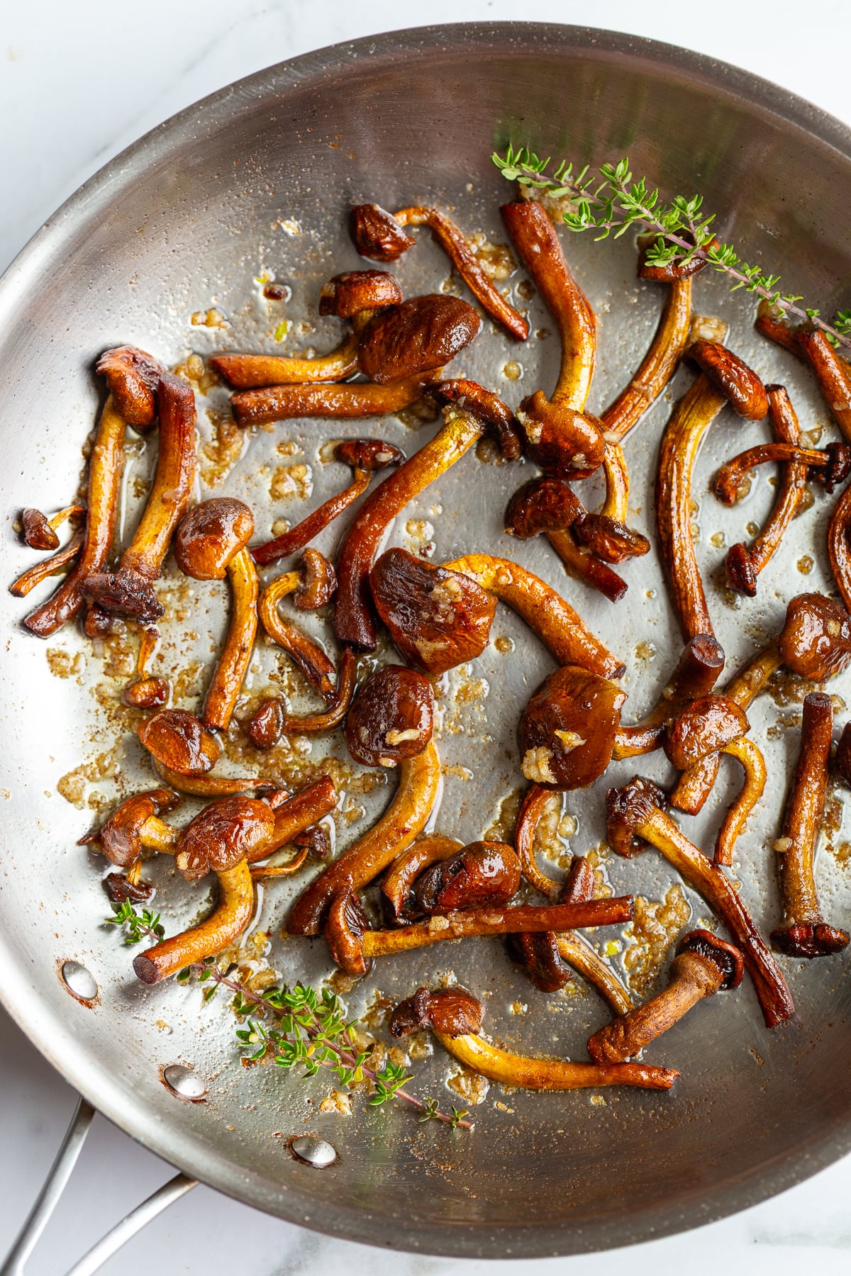 Caramelized chestnut mushrooms in a skillet with fresh thyme sprigs added