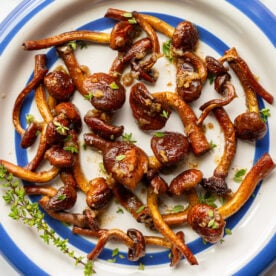 Sautéed chestnut mushrooms with golden-brown caramelization arranged on a blue-rimmed plate with fresh thyme