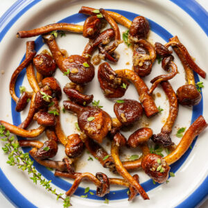 Sautéed chestnut mushrooms with golden-brown caramelization arranged on a blue-rimmed plate with fresh thyme