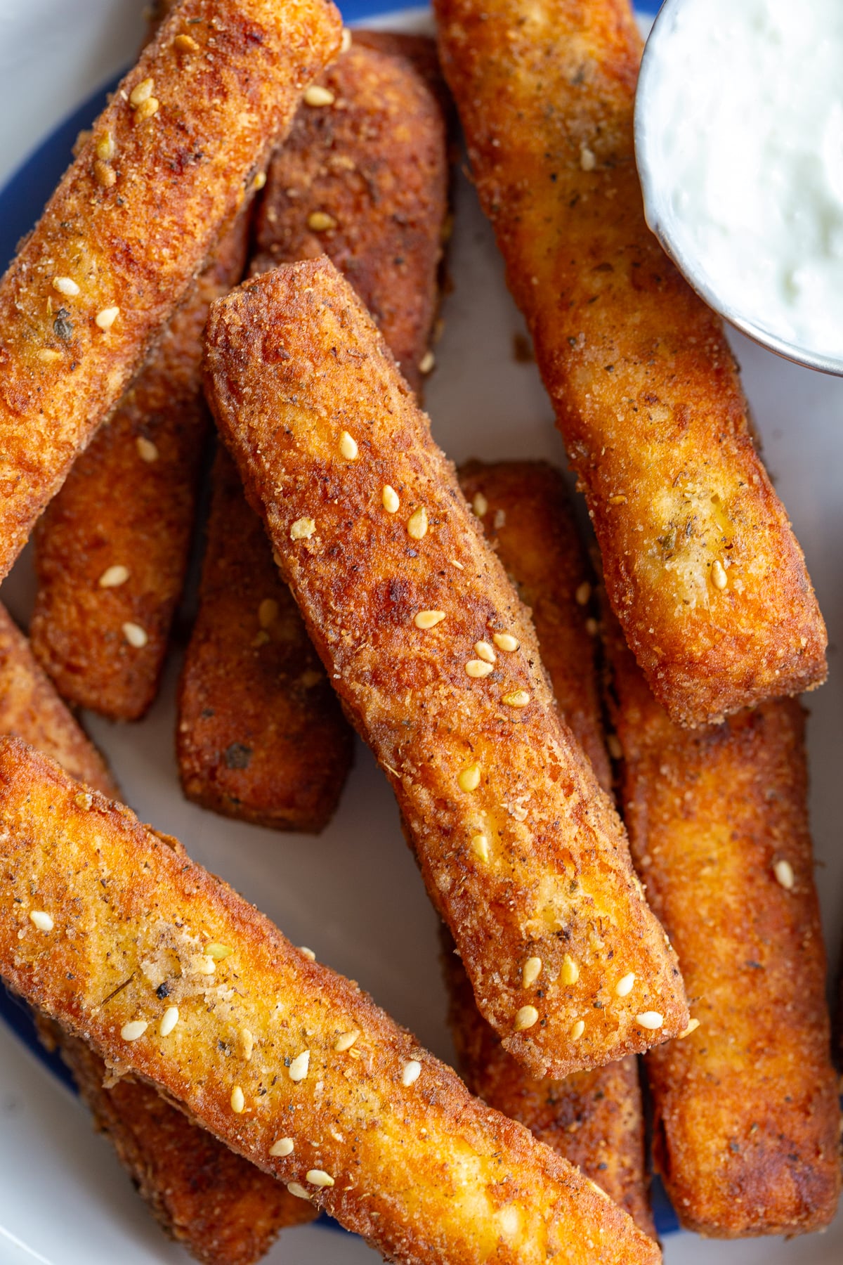 golden fried halloumi fries stacked on a plate with a bowl of yogurt dipping sauce on the side