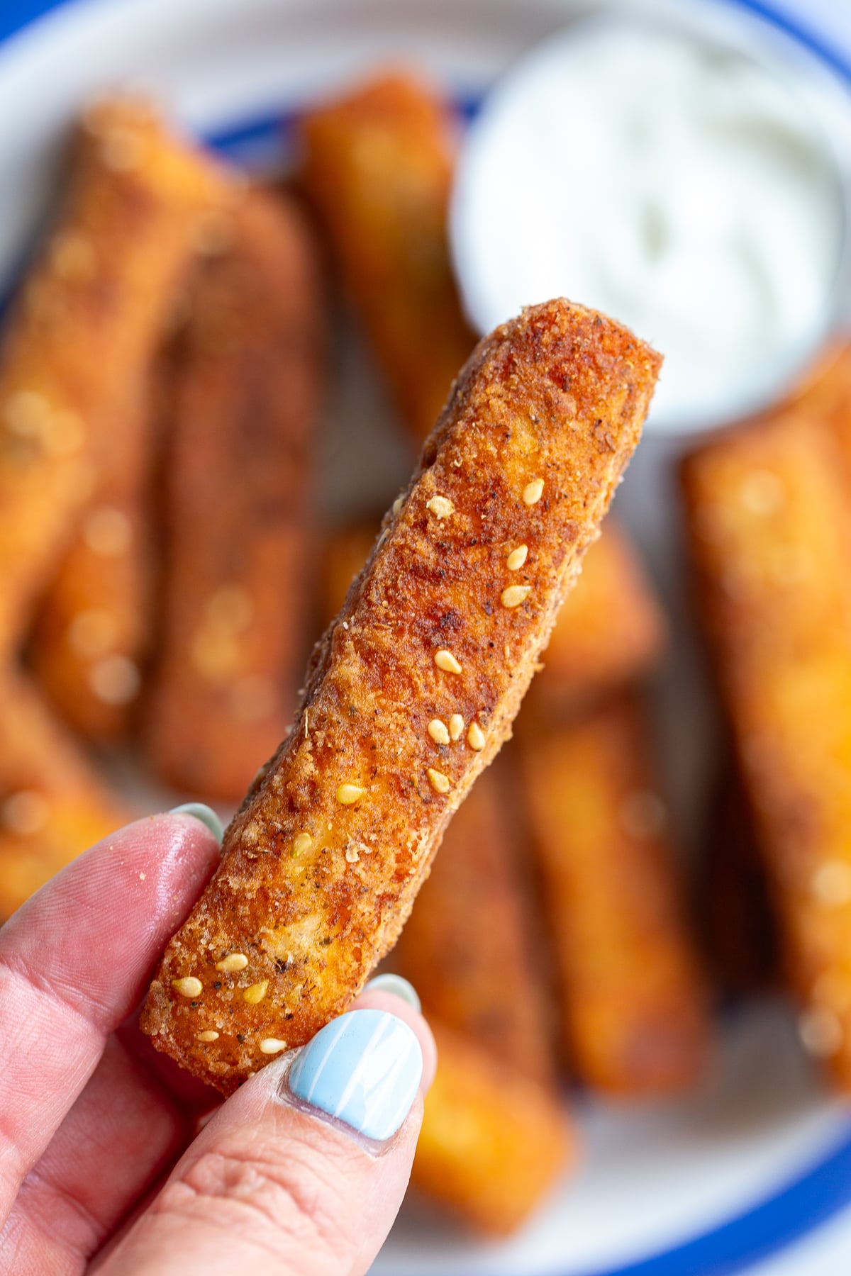golden fried halloumi fries stacked on a plate with a bowl of yogurt dipping sauce on the side