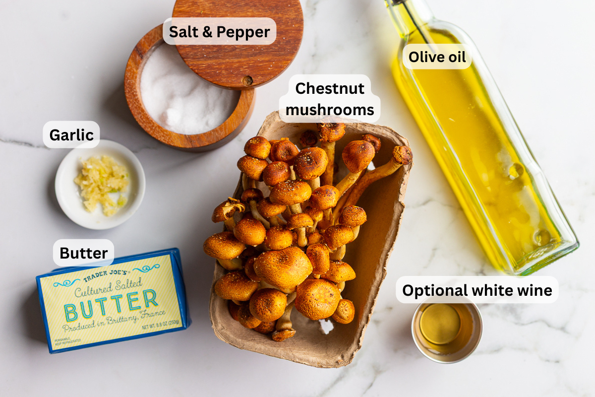 Overhead shot of chestnut mushroom ingredients labeled on a marble counter, including chestnut mushrooms, garlic, butter, olive oil, salt and pepper, and optional white wine