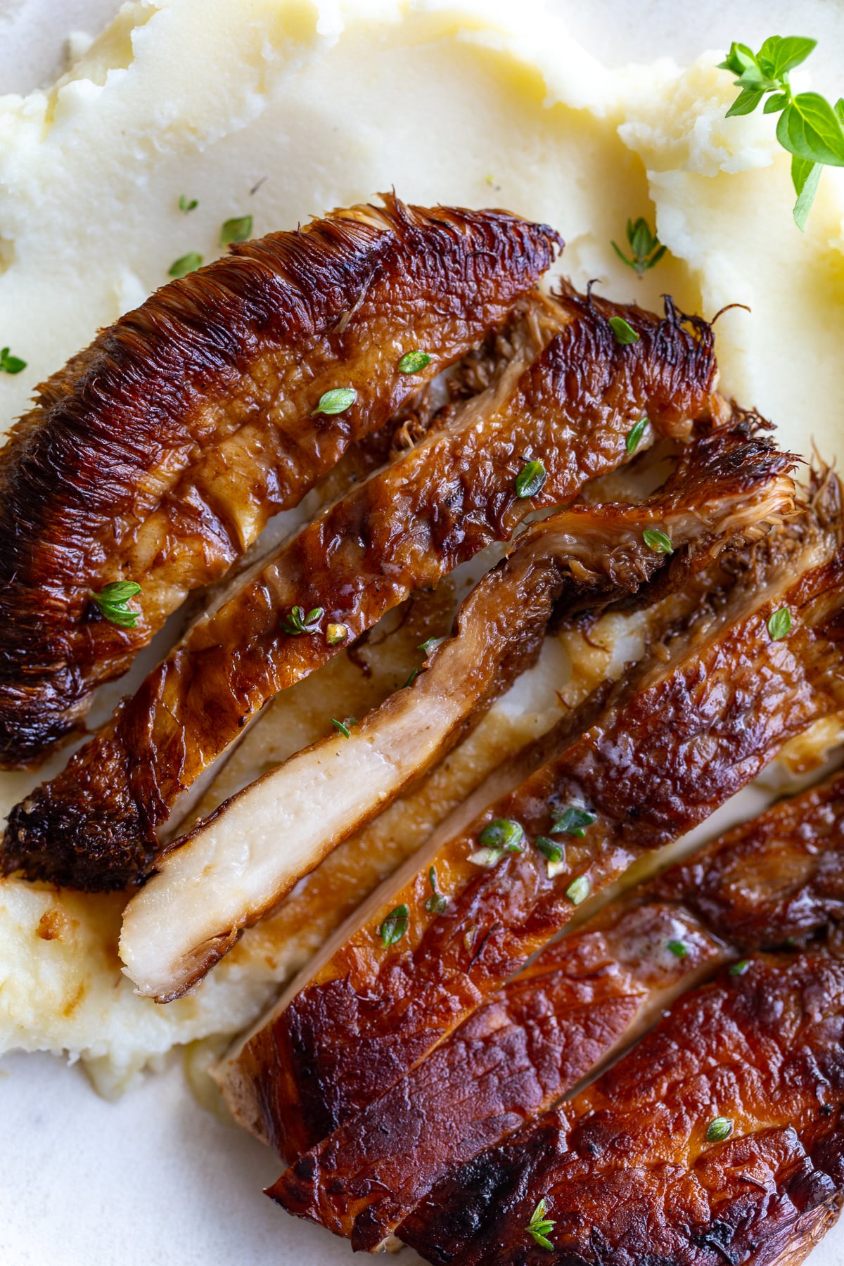 Close-up of sliced lion's mane steak pieces with a caramelized crust, garnished with fresh herbs, served over mashed potatoes