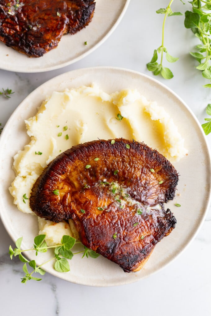 Seared lion's mane steak topped with melted garlic herb butter, served alongside mashed potatoes and garnished with fresh thyme