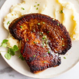 Overhead shot of lion's mane steak with garlic herb butter melting over the top, plated with mashed potatoes and fresh herbs