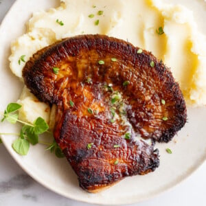 Overhead shot of lion's mane steak with garlic herb butter melting over the top, plated with mashed potatoes and fresh herbs