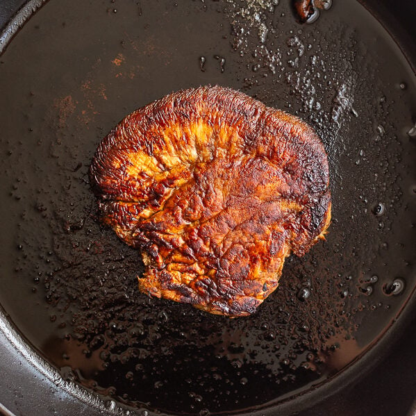 A lion's mane mushroom steak searing in a cast iron skillet with a golden-brown crust forming