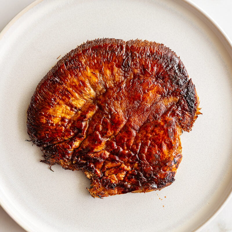 A seared lion's mane mushroom steak with a deep golden-brown crust on a white plate