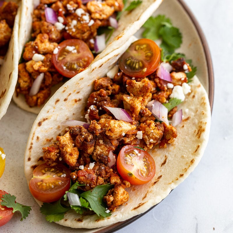 flour tortilla filled with tofu taco meat and topped with cherry tomatoes, cilantro, onion, and feta
